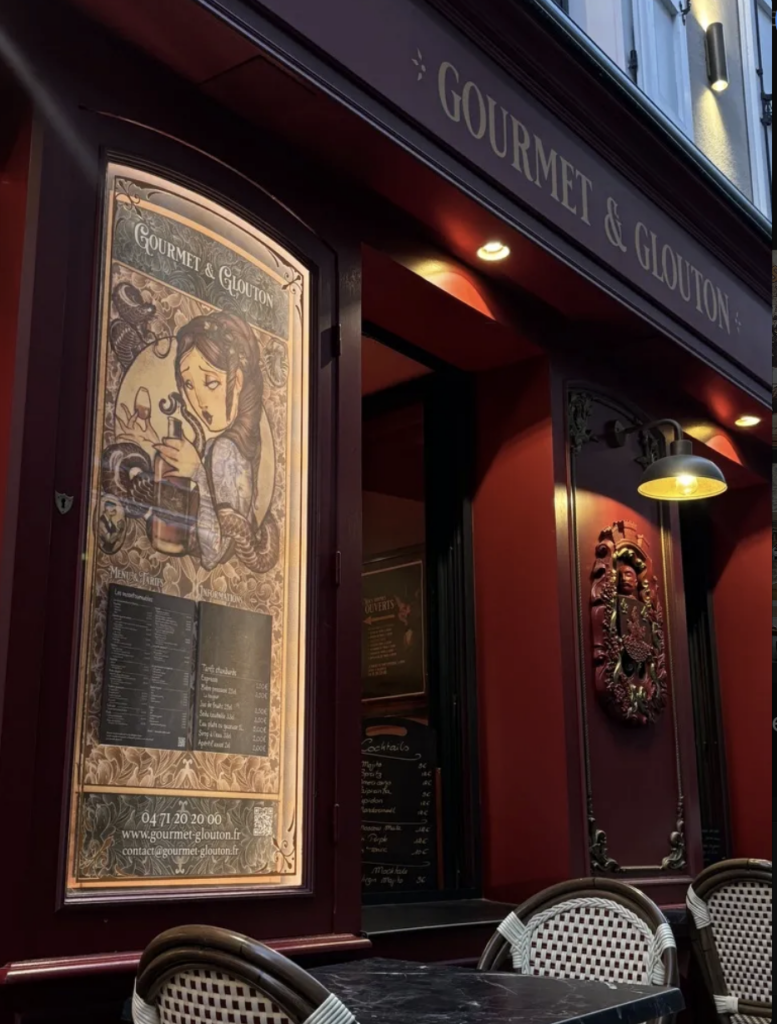 Façade de Gourmet & Glouton la nuit avec illustration Art Nouveau sur le menu, Chaudes-Aigues