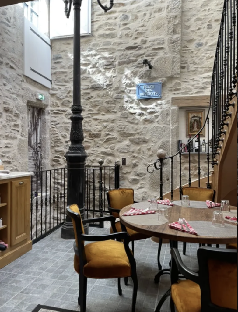 Intérieur de Gourmet & Glouton avec réverbère en fonte, escalier en fer forgé et chaises dorées, Chaudes-Aigues
