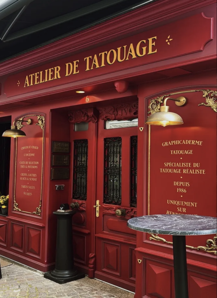 Façade rouge et or de l'atelier de tatouage Graphicaderme à Chaudes-Aigues, ornements Belle Époque et lettrage doré