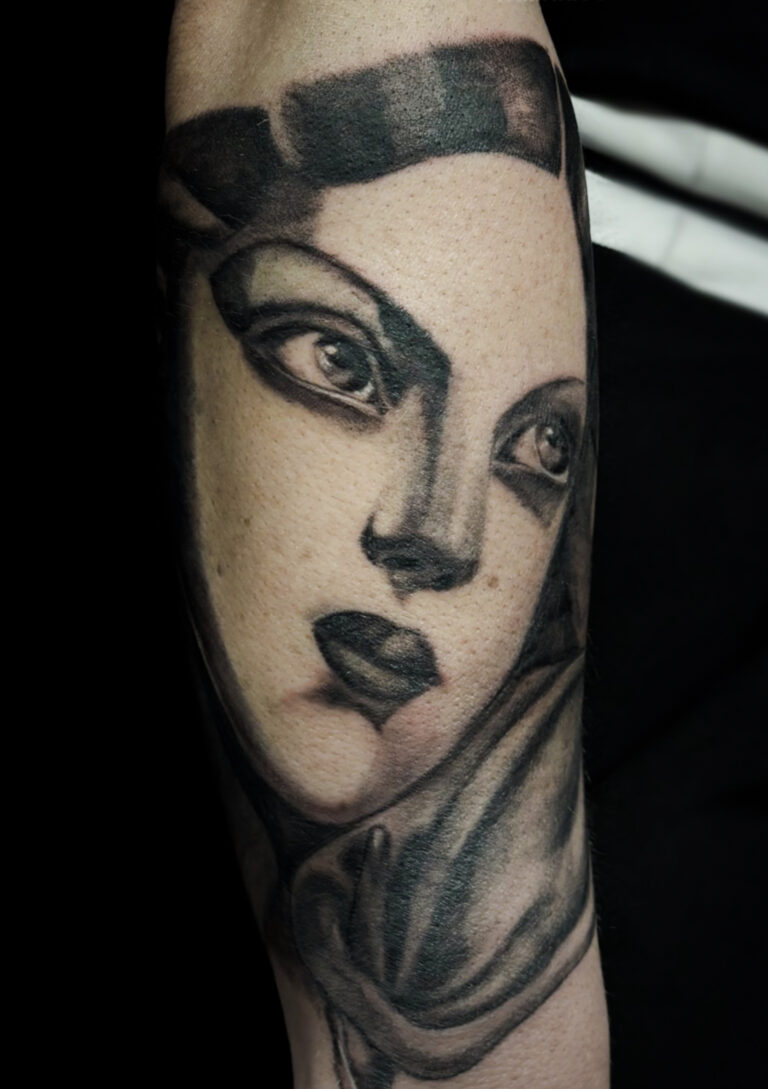 Tatouage de portrait féminin en noir et gris sur bras, inspiration art déco, volumes structurés, réalisé par Tamara Chaudesaigues.