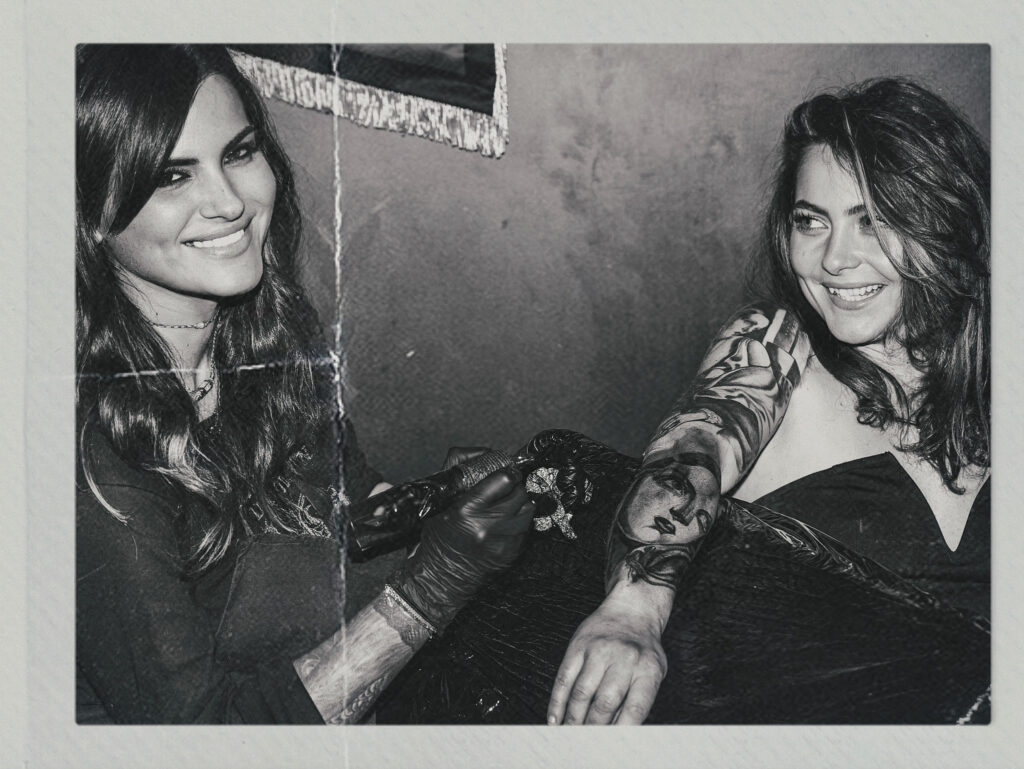 Tamara Chaudesaigues, tatoueuse, en séance de tatouage avec une cliente, portrait en noir et blanc, approche artistique et humaine, entre Avignon et la scène créative de Londres.