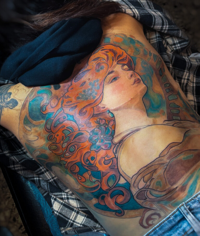 Tatouage féminin art nouveau en couleur sur le dos, lignes décoratives et palette chaude, inspiration Alphonse Mucha, réalisé par Tamara Chaudesaigues.