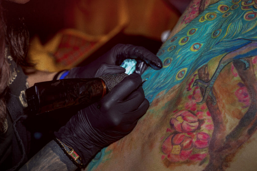Tatouage couleur Art nouveau en cours de réalisation, détail de plumes de paon et fleurs aux teintes vibrantes, réalisé à Avignon par Tamara Chaudesaigues