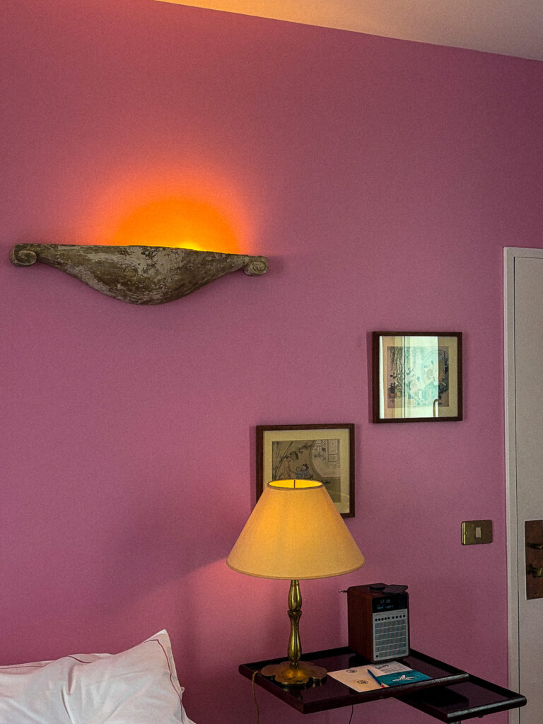Chambre rose de l’Hôtel Amour à Nice avec lampe murale et ambiance artistique chaleureuse