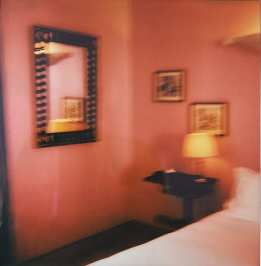 Chambre rose de l'Hôtel Amour Nice, miroir en bois, lampe de chevet dorée et tableaux aux murs
