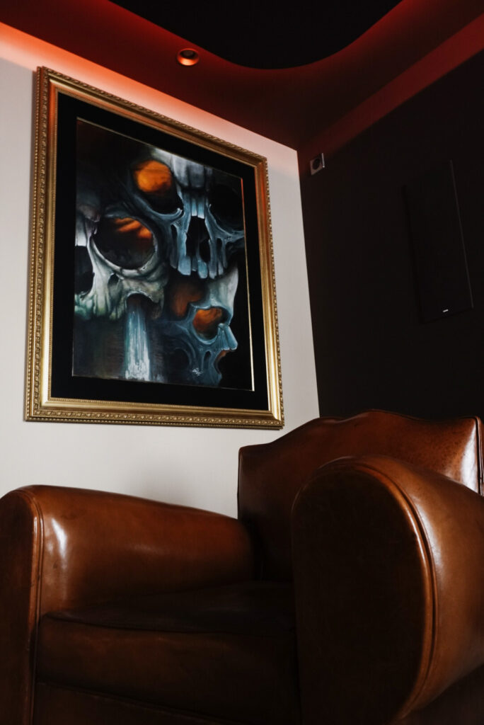 Fauteuil en cuir marron et peinture de Jeff Gogue encadrée dans le studio Graphicaderme Chaudes-Aigues, ambiance lumière rouge