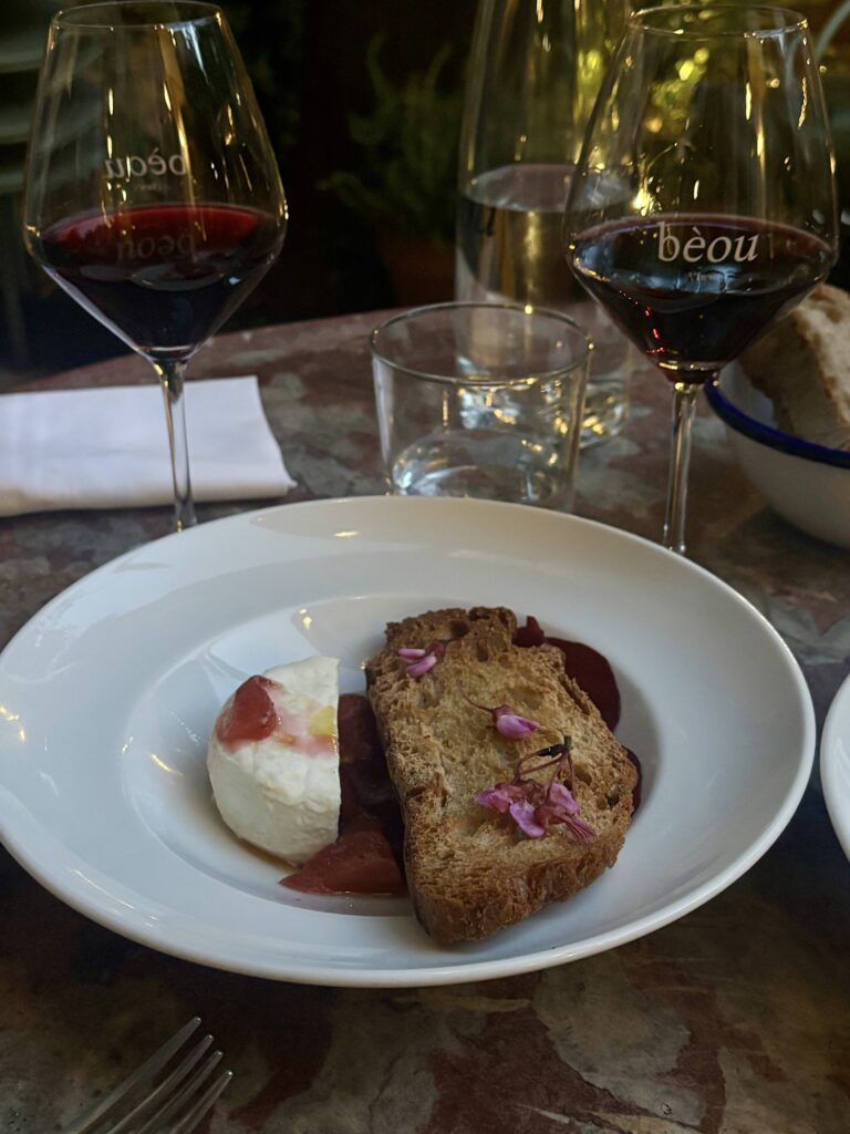 Fresh goat cheese toasted bread beetroot edible flowers at Le Bèou restaurant Avignon, red wine glasses on marble table