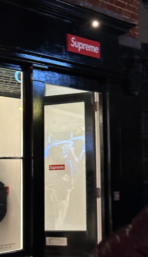 Façade de la boutique Supreme à Soho Londres la nuit, logo rouge sur fond noir