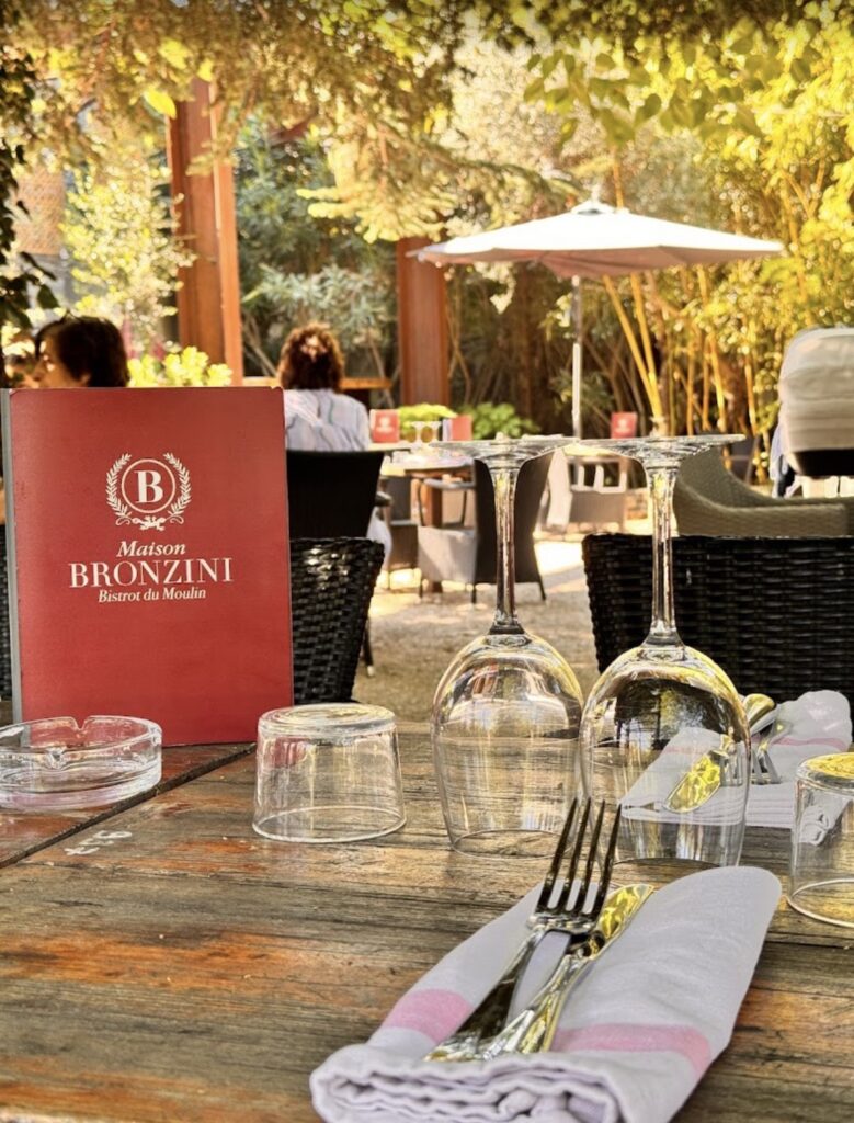 Terrasse de la Maison Bronzini Bistrot du Moulin à Villeneuve-lès-Avignon, menu rouge, verres à vin, table en bois sous les arbres