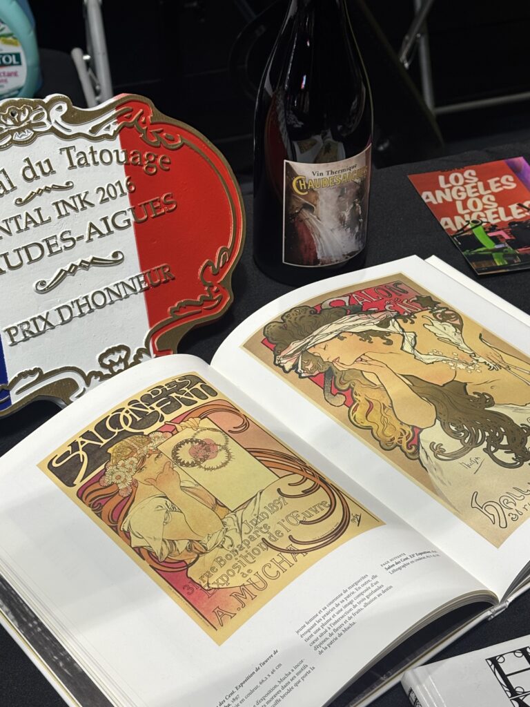 Alphonse Mucha artwork book open on Tamara Chaudesaigues's convention table, Prix d'Honneur Chaudes-Aigues Tattoo Festival 2016