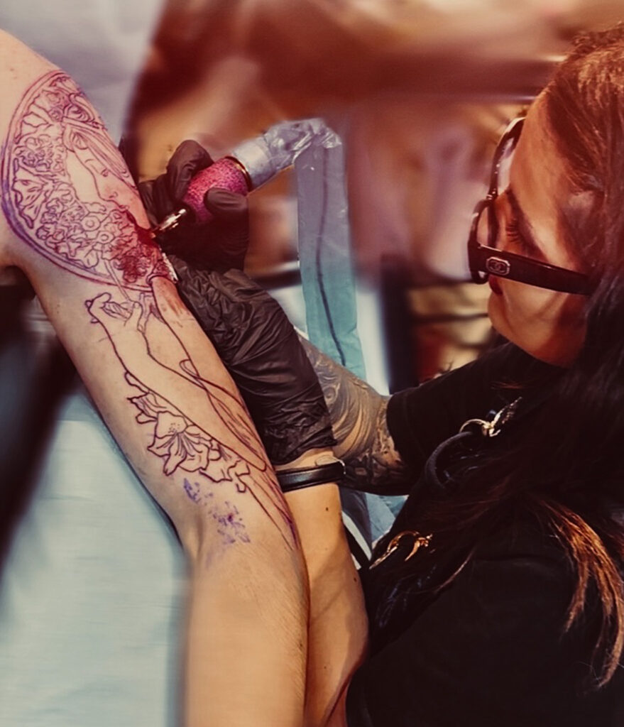 Tamara Chaudesaigues Art Nouveau tattoo artist tattooing a full arm inspired by Mucha, Graphicaderme Avignon
