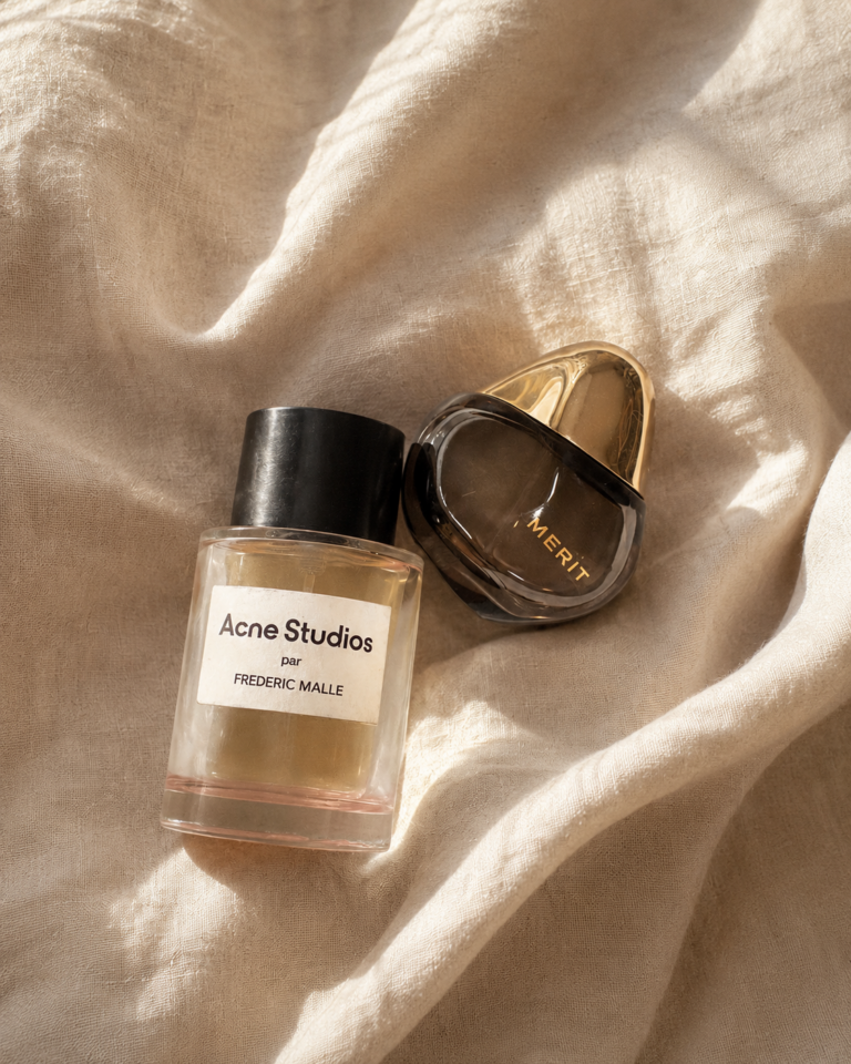 Les Parfums de Tamara Chaudesaigues, Acne Studios par Frédéric Malle et Retrospect de Merit photographiés sur un tissu beige à la lumière naturelle.