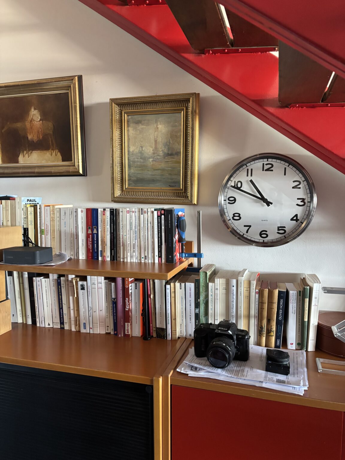 Books, vintage camera and paintings under the red staircase of a duplex in the Cité Radieuse