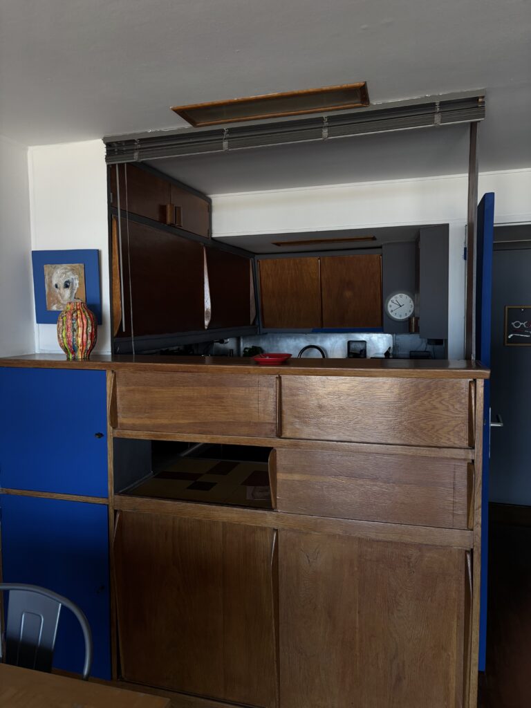 Cuisine ouverte avec rangements en bois et panneaux bleus dans un duplex habité de la Cité Radieuse
