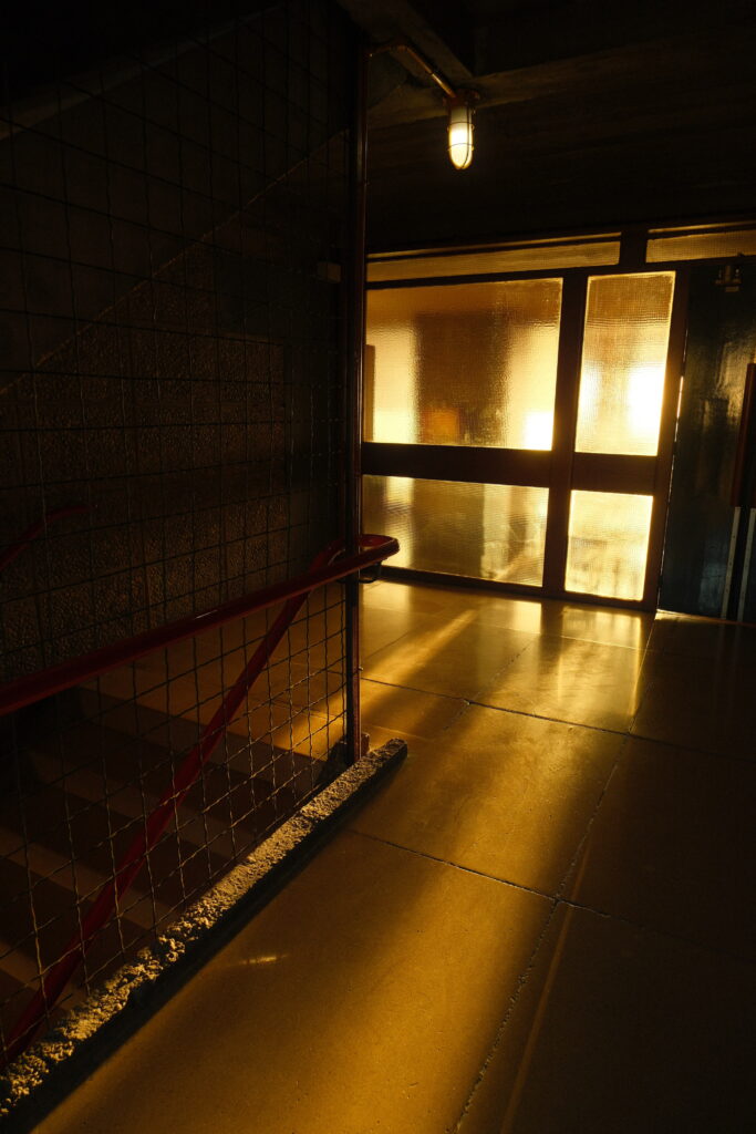 Lumière dorée traversant une porte vitrée dans un couloir sombre de la Cité Radieuse