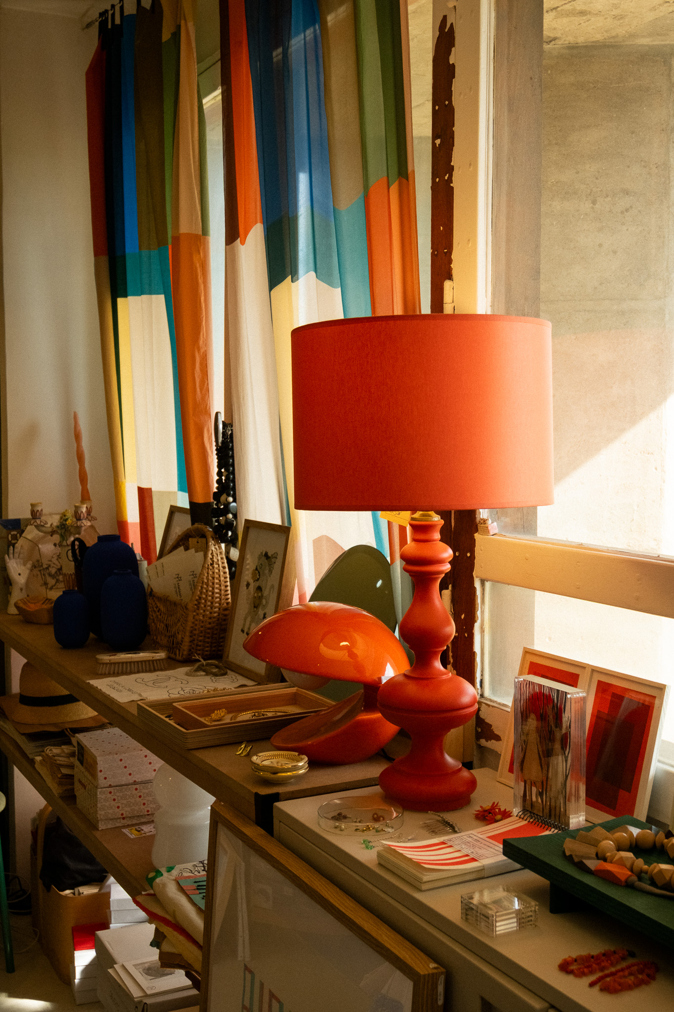 Lampes rouges, bijoux, carnets et rideaux colorés dans la boutique Maison Mirbel