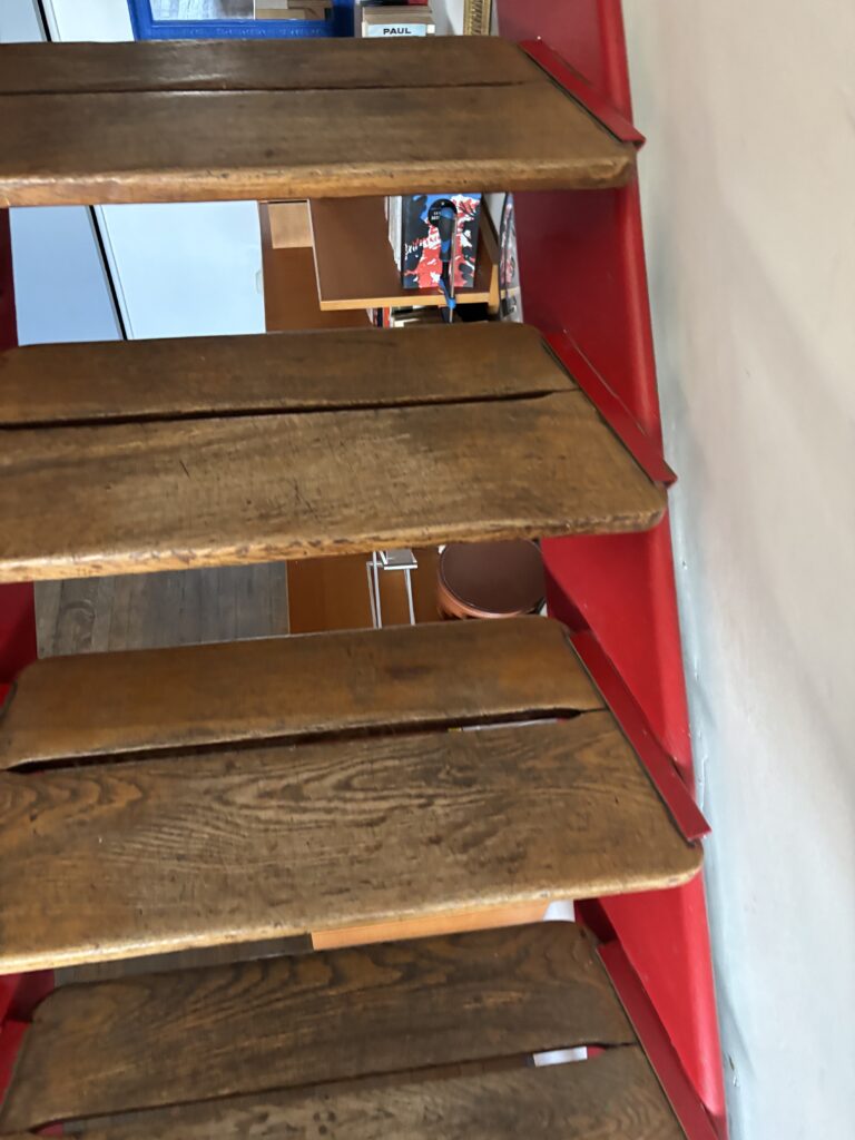 Vue à travers les marches en bois et la structure rouge de l’escalier d’un duplex de la Cité Radieuse