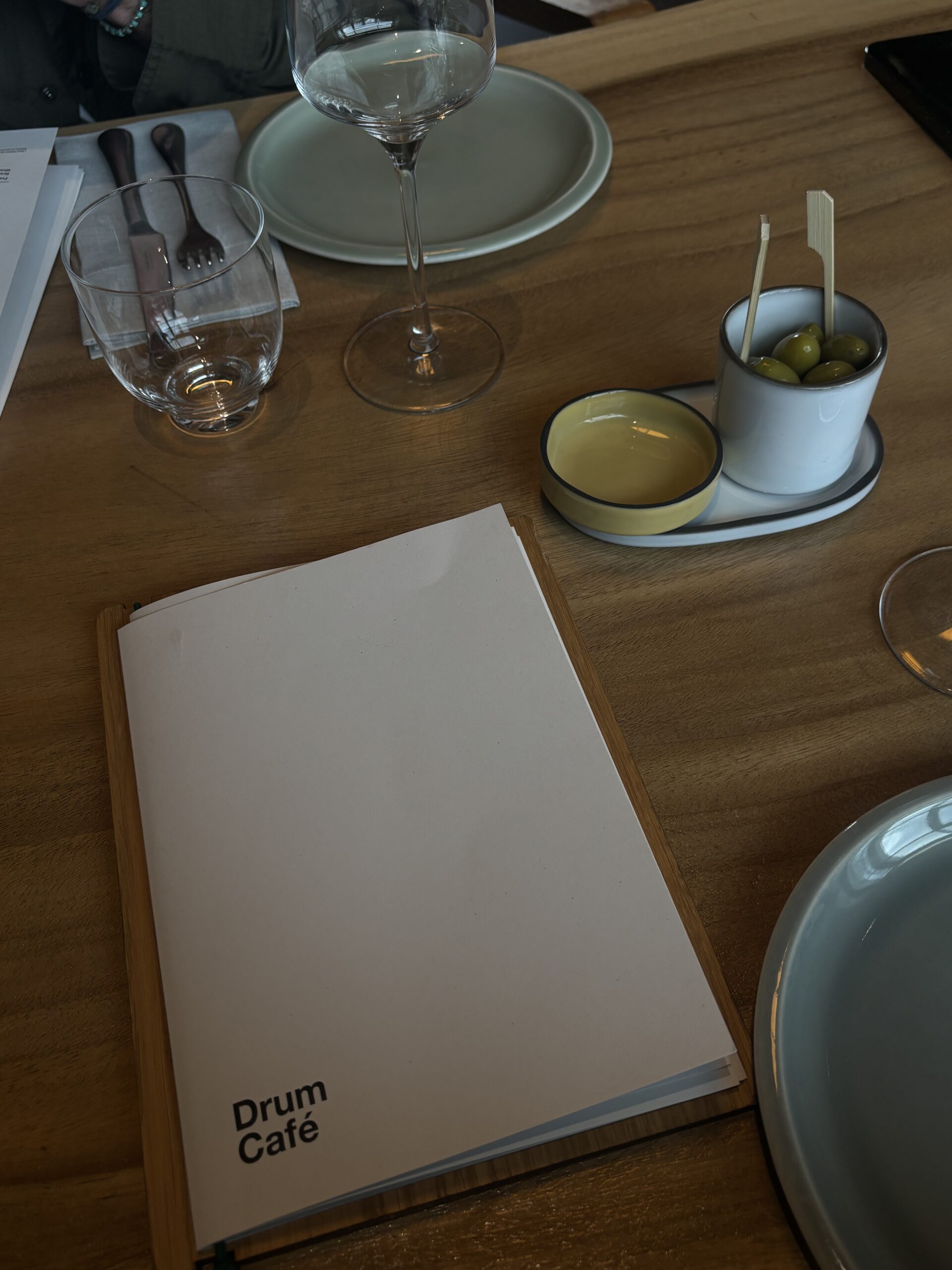 Carte du Drum Café posée sur une table en bois avec des olives et des verres