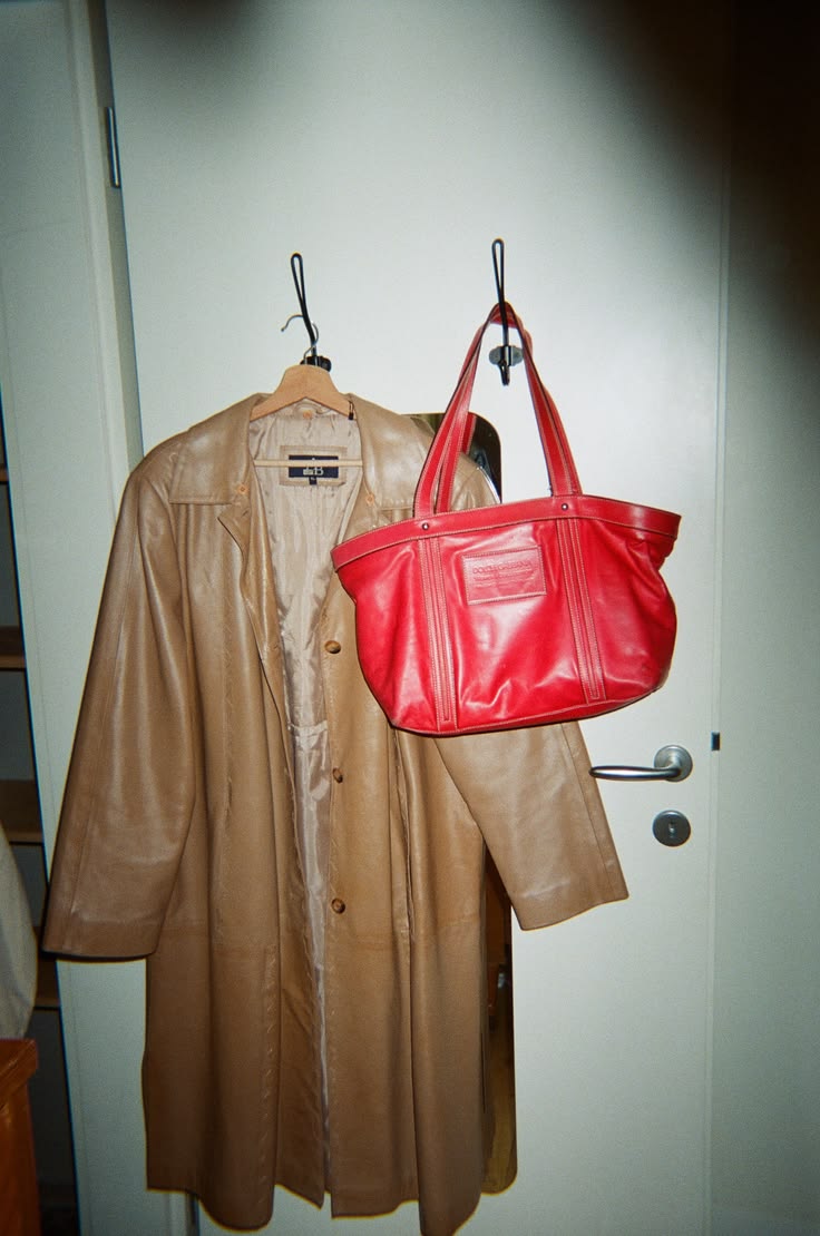 A long beige leather coat and red bag hanging in a wardrobe