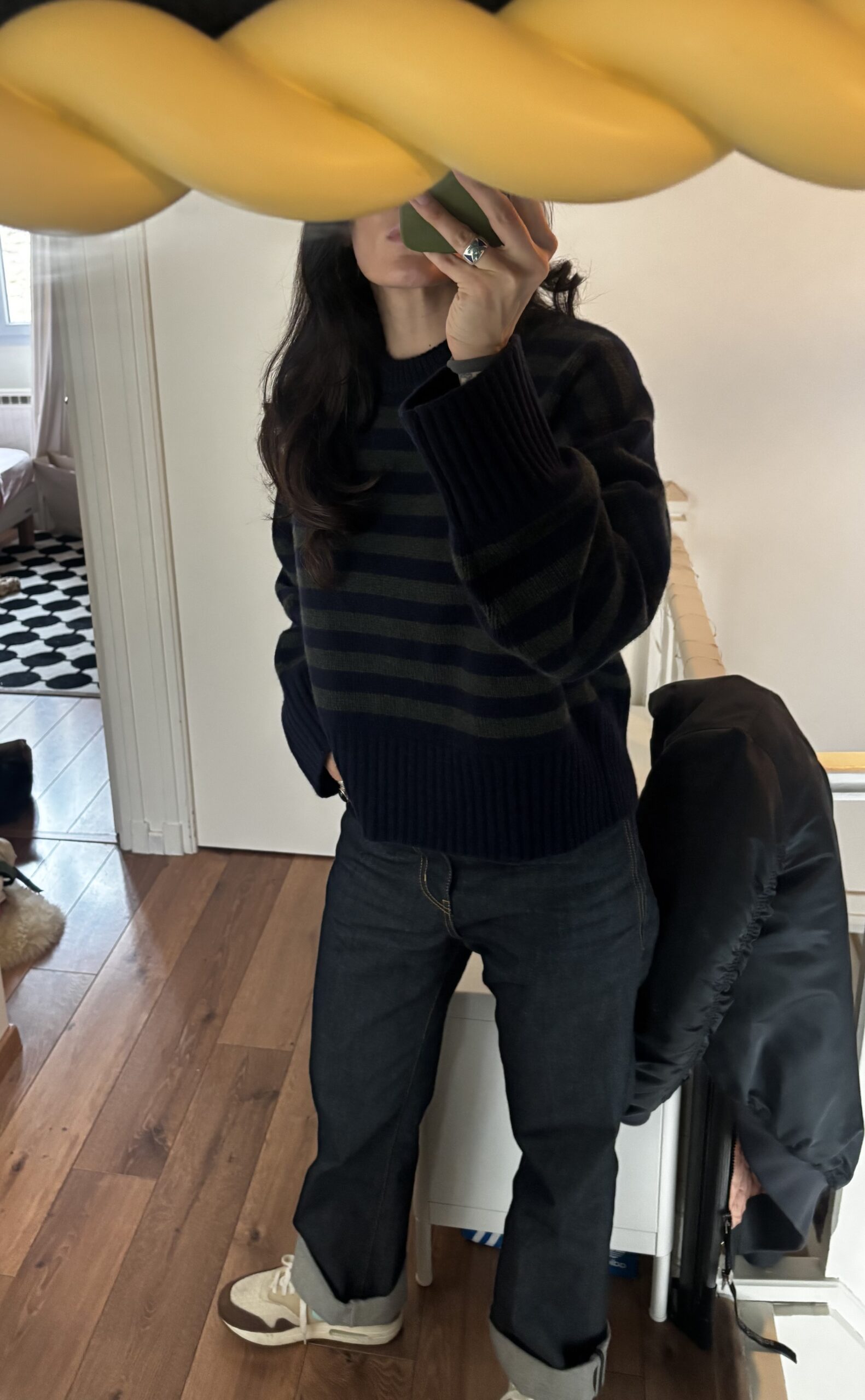 Close-up view of the blue and green striped Skall Studio sweater worn with Saint Laurent jeans.